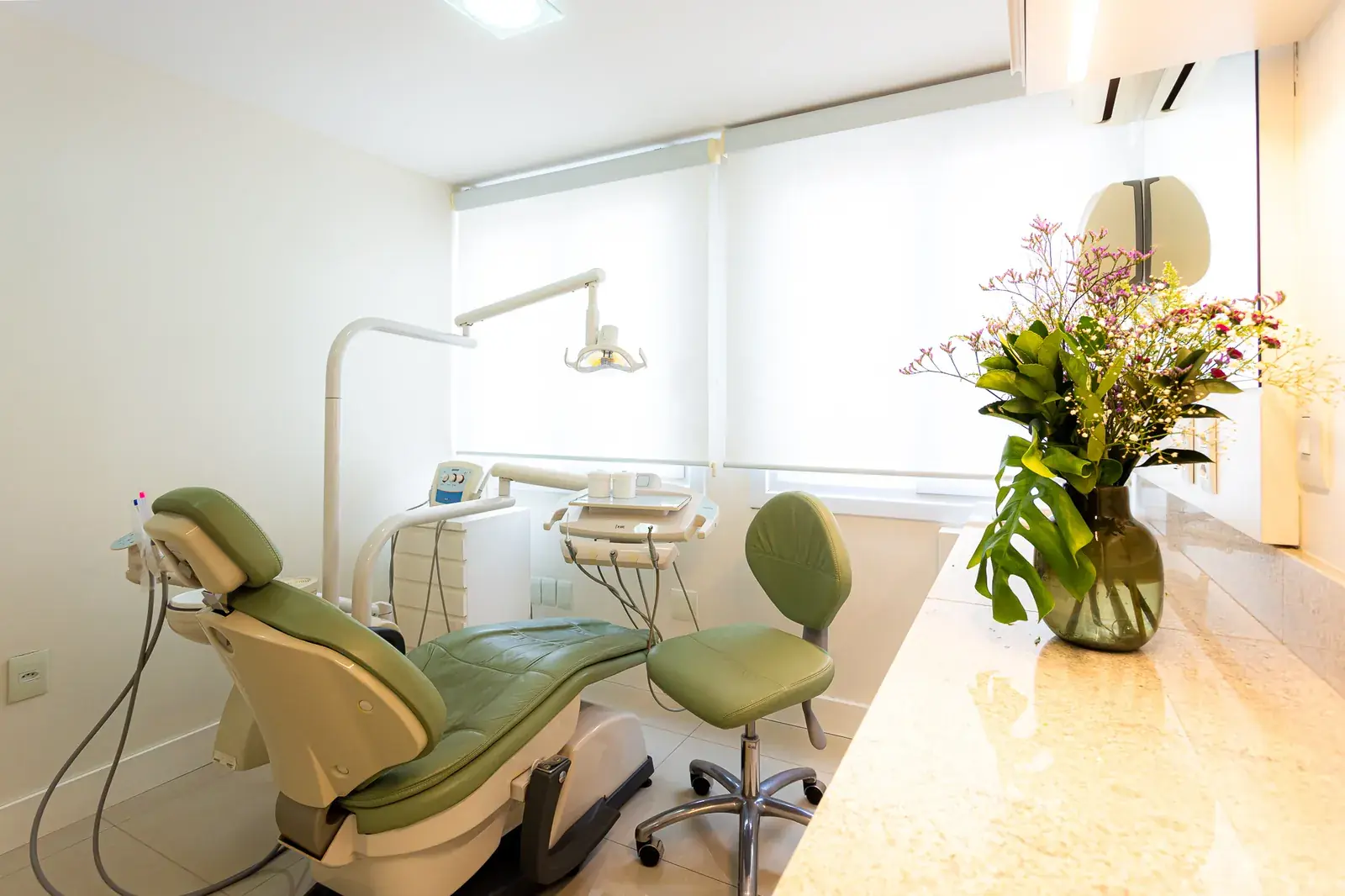 Sala de procedimento da Migliore Odontologia, com poltrona verde-sálvia e flores
